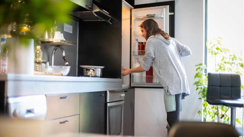vrouw staat in keuken en opent koelkast